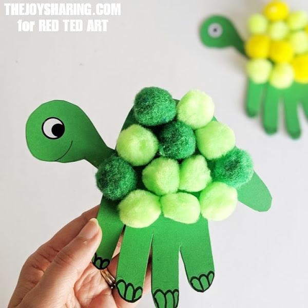 Construction paper handprint with pom poms on the palm and turtle head on the side.